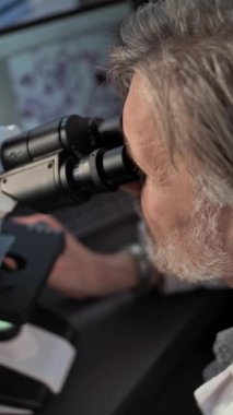 Olgun mikrobiyolog mikroskop altında fosil analizi yapar, laptop ekranındaki mikroorganizmalara bakar. Bilim adamı, arkeoloji laboratuvarında gelişmiş ekipmanlarla çalışıyor. Dikey çekim