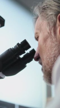 Fosil örneğini mikroskop altında analiz ederek bilimsel araştırma yapan olgun bilim adamının dikey görüntüsü. Mikrobiyolog arkeoloji laboratuvarında gelişmiş ekipmanlarla çalışıyor. Bilimsel yöntem