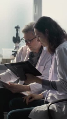 Laboratuvar önlüklü erkek ve kadın bilim adamları bilimsel araştırmalar yapıyor, kağıtlara bakıyor ve tablet bilgisayar kullanıyorlar. Paleontologlar veya arkeologlar ileri arkeoloji laboratuvarında çalışırlar..