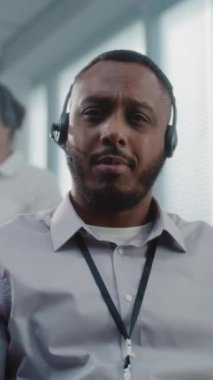 Çağrı merkezi: Dost canlısı Afrikalı Amerikalı teknik müşteri destek uzmanının dikey portresi, kulaklık takıyor, kameraya bakıyor. Acil durum operatörleri ekibi beklemede.