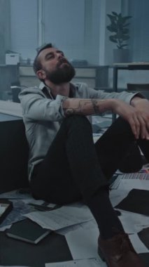 Depresyondaki iş adamının başarısız iş anlaşmasından ya da kötü haber almasından dolayı öfkeli bir şekilde yerde oturduğu dikey çekim. Mahvolmuş ofis odasında stresli bir ofis çalışanı. Finansal kriz ya da kovulma