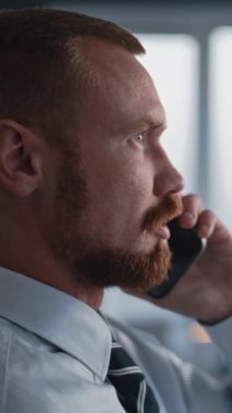 Modern kurumsal ofiste çalışan yetişkin bir adamın dikey görüntüsü: Profesyonel finans uzmanı veya bankacı iş müşterisiyle telefonla iletişim kurar ve proje, mali anlaşma veya