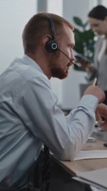 Dikey çekim yapan bir borsacı ya da borsacı bilgisayar başında çalışıyor, iş müşterisiyle telefonda görüşüyor, borsayı izliyor, notlar alıyor. Arka plandaki bayan meslektaşım..