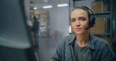 E-ticaret deposu ya da postane: Müşteriyle kulaklıkla yapılan lojistik konuşmalarda kadın müşteri destek uzmanı, bilgisayar kullanır. Merkez çalışanı dağıtım için kutucukları işaretliyor.