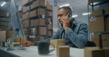 Sıralama merkezi: Afrikalı Amerikalı perakende satıcısı veya lojistik müdürü müşteriyle cep telefonuyla konuşur, teslimat için bilgisayarda paket bilgilerini kontrol eder. E-ticaret emriyle depo ya da depo..