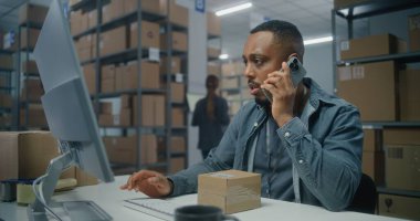 Posta servisi deposu veya E-ticaret mağazası: Afro-Amerikan lojistik koordinatörü telefonla konuşur, paketleri kontrol eder, bilgisayar kullanır. Sıralama merkezi çalışanı karton kutularla çalışır.