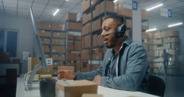 Afro-Amerikan lojistik koordinatörü, telefonda müşteriyle kulaklık sohbeti yapıyor, bilgisayar kullanıyor, posta servisinde ya da E-ticaret deposunda çalışıyor. Merkez çalışanı karton kutuları kontrol ediyor.