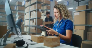 Kadın depo görevlisi, müşterilere gönderilecek paketleri hazırlamak için tablet bilgisayar kullanarak paketleri tarıyor. Karton kutular taşıyan tasnif merkezi çalışanları. Postane veya çevrimiçi mağaza deposu.