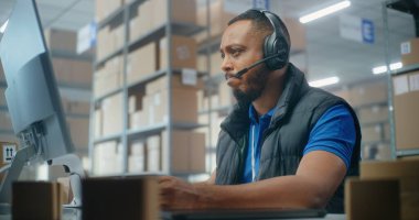 Müşteriyle kulaklık takan Afro-Amerikan lojistik koordinatörü, bilgisayar kullanıyor, postanede ya da e-ticaret deposunda çalışıyor. Teslimat için karton kutular taşıyan tasnif merkezi çalışanları.