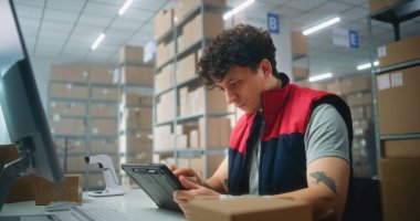 Depodaki erkek tezgahtar paketleri tablet bilgisayar kullanarak tarıyor, posta servisinde ya da çevrimiçi mağaza lojistik deposunda çalışıyor. Teslimat için karton kutular taşıyan tasnif merkezi çalışanları. E-ticaret ürünleri