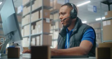 Müşteriyle kulaklık takan Afro-Amerikan lojistik koordinatörü, bilgisayar kullanıyor, postanede ya da e-ticaret deposunda çalışıyor. Teslimat için karton kutular taşıyan tasnif merkezi çalışanları.