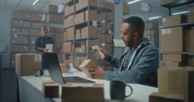 Afrikalı Amerikalı lojistik müdürü barkod tarayıcı ile paketleri tarar, iş arkadaşıyla konuşur, dizüstü bilgisayar kullanır. Teslimat için kutu taşıyan tasnif merkezi çalışanı. E-ticaret mağazası veya postanenin deposu.