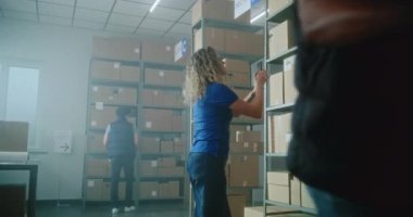 Çevrimiçi mağazanın deposunda çalışan çok ırklı çalışanları sınıflandırıyor. Kadın lojistik uzmanı akıllı telefon kullanarak karton kutuda kod taraması yapıyor. Müşterilere nakliye için malları kontrol ediyor..