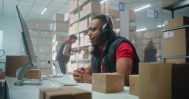 Afro-Amerikalı müşteri destek uzmanı, çağrı cihazını kullanarak, bilgisayar kullanarak, postanede ya da çevrimiçi depolamada çalışıyor. İşçiler karton kutulara bakıyor..