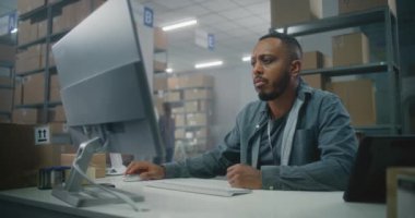 Afrika kökenli Amerikalı lojistik uzmanı depo tesislerindeki bilgisayarda çalışıyor. Kadın envanter memuru karton parseldeki kodu tarayıcı kullanarak tarıyor. Posta servisi veya E-ticaret mağazası sıralama merkezi.