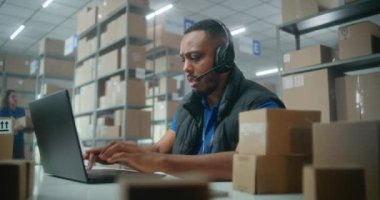 Kulaklıktaki Afrikalı Amerikalı perakendeci ya da lojistik koordinatörü müşteriyle konuşur, posta servisi ya da çevrimiçi depolama deposunda dizüstü bilgisayarda çalışır. Karton kutular taşıyan tasnif merkezi çalışanları