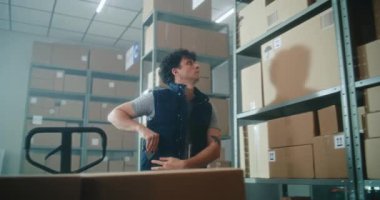 Erkek envanter müdürü akıllı telefon kullanarak pakette kod taraması yapar. Depo tesisinde karton kutularla dolu palet kamyonuna yükler. Arka planda çalışan tasnif merkezi çalışanları. Teslimat servisi.
