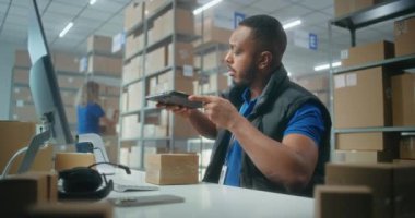 Afro-Amerikalı depo görevlisi paketleri tablet bilgisayar kullanarak tarıyor, postanede çalışıyor. Nakliye için karton kutular taşıyan tasnif merkezi çalışanları. Çevrimiçi mağaza ürünleriyle lojistik depolama