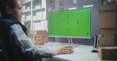 Dağıtım Merkezi: Depo Tesisindeki Bilgisayar üzerine Kadın Lojistik Uzmanı Çalışıyor, Veri Giriyor, Envanter Kontrol ya da Paketler Bilgilerini Denetliyor. PC Ekranı Yeşil Ekran Krom Anahtarı gösteriyor. Doli Vuruşu.