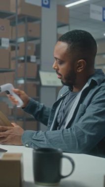 Afrikalı Amerikalı lojistik müdürü barkod tarayıcı ile paketleri tarar, iş arkadaşıyla konuşur, dizüstü bilgisayar kullanır. Teslimat için kutu taşıyan tasnif merkezi çalışanı. E-ticaret mağazasının deposu. Dikey çekim.