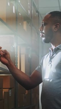 Afro-Amerikan Sınıflandırma Merkezi, Smartphone ile Depo Tesisi 'nde E-Ticaret Siparişi ile birlikte karton kutuları tarıyor, Müşteriye Sevkiyat İçin Paket Getiriyor. Posta Teslimat Servisi. Dikey Çekim