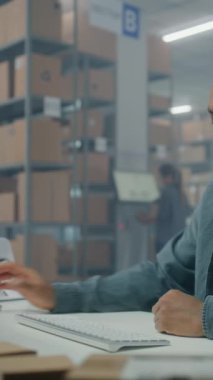Afro-Amerikan lojistik posta servisi çalışanı online siparişleri kontrol eder, bilgisayarla çalışır. Sıralama merkezi kadın çalışanı teslimat için paketleri kontrol ediyor. Depo ya da dağıtım merkezi. Dikey çekim.