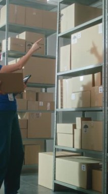 Erkek depo çalışanı karton kutuyu rafa koyuyor. Kadın envanter yöneticisi tablet bilgisayar kullanıyor, parseldeki kodları tarıyor. E-ticaret çevrimiçi emirleri olan lojistik merkezi. Dikey çekim.