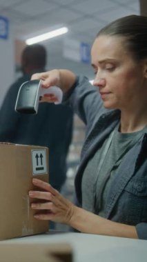 Kadın envanter müdürü paketleri barkod tarayıcı ile tarar, müşteriye nakliyeye hazırlanır, bilgisayarda çalışır. Depo çalışanı kutuları işaretliyor. E-ticaret mağazası veya posta servisi. Dikey çekim.