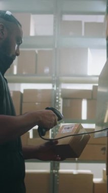 Afro-Amerikan Lojistik Müdürü Posta Terminalindeki Karton Kutuyu Dijital Ekran ile Tarıyor, E-Ticari Mallar İzleme Uygulamasını kullanarak Paketin Bilgilerini Kontrol Ediyor. Depo Merkezi. Dikey Çekim.