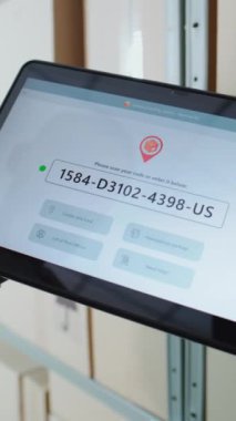 Posta Deposu İşçisi, Karton Kutudaki QR kodunu tarayıcı ile tarar, Paket Bilgilerini izler. Tablet Bilgisayar Ekranı Paket Yönlendirmesini Kontrol Etmek için Sevkiyat İzleme Yazılımını gösterir. Dikey Çekim.