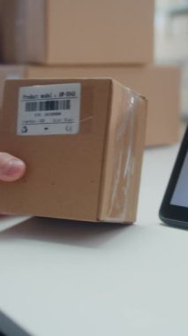 Envanter Yöneticisi, Tarayıcı ile karton kutudaki kodu tarar, Paket Bilgilerini kontrol eder. Tablet Bilgisayar Ekranı Çevrimiçi Siparişlerle Paket İzleme Sistemi 'ni gösterir. Dikey Çekim.