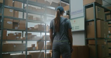 High-Tech Advanced Sorting Center: Warehouse Worker in Futuristic Full Body Robotic Exoskeleton Walks with Heavy Cardboard Box. Female Logistics Specialist Scans Parcel, Checks Shipping Information. clipart