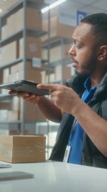 Afro-Amerikalı depo görevlisi paketleri tablet bilgisayar kullanarak tarıyor, postanede çalışıyor. Nakliye için karton kutular taşıyan tasnif merkezi çalışanları. Çevrimiçi mağaza ürünleriyle lojistik depolama