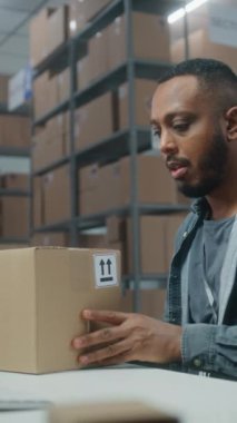 Posta servisi: Afro-Amerikan lojistik uzmanı tarayıcı ile paketleri tarar, müşteriye teslimata hazırlanır, bilgisayar kullanır. Tasnif merkezi çalışanı kutuları taşıyor. E-ticaret emirleri. Dikey çekim.