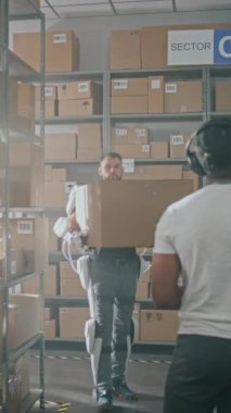 Yüksek Teknoloji Deposu: Afro-Amerikan Envanter Uzmanı Tablet Bilgisayar Envanter Kontrol. Tam Vücut Robotik Dış iskelet Tasnif Merkezi İşçisi Rafa Karton Kutusunu Yerleştirdi. Dikey Çekim.