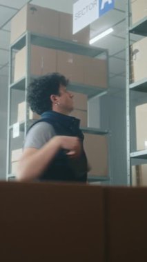 Depo çalışanı akıllı telefon kullanarak parseldeki kodları tarıyor, kutularla dolu bir palet kamyonu yüklüyor, itiyor. Arka planda çalışan depo çalışanları. Lojistik dağıtım merkezi. Dikey çekim.