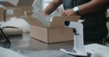 Afro-Amerikan Depo Katibi, içinde Online Order, Tarama Kodu, Tablet Bilgisayar, Nakliyeye Hazırlık Paketleri olan Karton Paketler. E-ticaret mağazası tasnif merkezi, teslimat servisi. Kapat.