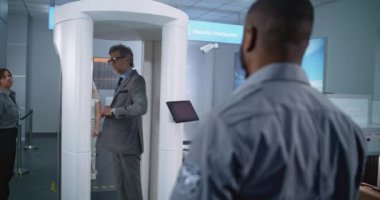 Havaalanı Terminal Güvenlik Kontrolü: Olgun İşadamı Metal Detektör Tarayıcısından Geçiyor. Afro-Amerikan Güvenlik Subayı, Yolcuyu Uçuş için Denetliyor. Çeşitli Gezginler Seyahate Çıkıyor.
