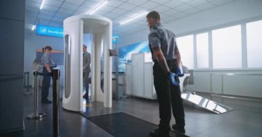 Havaalanı Güvenlik Kontrol Noktası: İşadamı bavulunu taşıma bandına yerleştirdi, Metal dedektörü tarayıcı kapısından geçti. Güvenlik görevlisi yolcuları uçuş için kontrol ediyor. Bir grup turist seyahate çıkıyor..