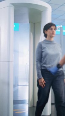 Havaalanı Terminali: Metal dedektör kapısından geçen kadın güvenlik kontrol noktasında. Kadın Güvenlik Görevlisi, Yolcu 'yu Uçak Uçuşu için Kontrol Ediyor. Tatil gezilerine çıkan turistler. Dikey Çekim.