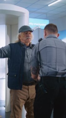 Uluslararası Havalimanı Terminalindeki Güvenlik Kontrolü Sırasındaki Yaşlı Adam: Uçağa binen yolcu için Güvenlik Görevlisi Yolcuyu Denetliyor. Arka planda, çeşitli gezginlerin kuyruğu Tatile çıkıyor