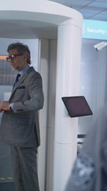 Havaalanı Terminal Güvenlik Kontrolü: İşadamı Metal Detektör Tarayıcısından Geçiyor. Afrikalı Amerikalı Güvenlik Subayı, Uçuş Yolcusunu Denetliyor. Çeşitli Gezginler Seyahate Çıkıyor. Dikey Çekim.