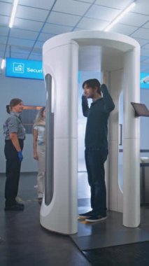 Havaalanı güvenlik kontrolü: Metal dedektör tarayıcısından geçen çeşitli yolcular, taşıyıcı banttan bavulları alıyor. Güvenlik Subayları, Gezginler Grubu, İnsanların Taranmasını Kontrol Ediyor. Dikey Çekim.