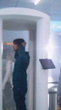 Havaalanı Terminali: Adam Metal Detektör Kapılarından Güvenlik Kontrol Noktasında Geçiyor. Güvenlik görevlisi yolcuları denetliyor, evrakları ve biletleri kontrol ediyor. Tatile çıkan çeşitli turistler. Dikey Çekim.