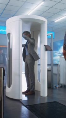 Havaalanı güvenlik kontrolü: Olgun adam metal dedektör tarayıcısından geçer, çantayı konveyör bandından alır. Güvenlik görevlisi, Yolcuyu Uçak Uçuşu için Kontrol Ediyor. Seyahate çıkan gezginler. Dikey Çekim.