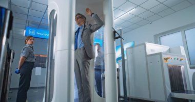 Havalimanı Terminali 'ndeki metal dedektör kapısından geçen çeşitli insanlar. Güvenlik Subayı, Uçak Uçuşu Yolcularının Denetimini Kontrol Ediyor. Bir grup Gezgin Tatile Çıkıyor. El bilgisayarı.