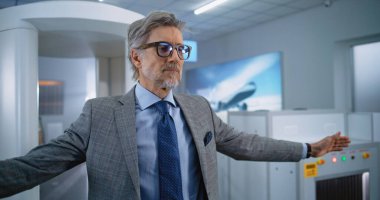 Havaalanı Terminal Güvenlik Kontrolü: Olgun İşadamı Metal Detektör Tarayıcısından Geçiyor. Afro-Amerikan Güvenlik Subayı, Yolcuyu Uçuş için Denetliyor. Çeşitli Gezginler Seyahate Çıkıyor.