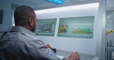 Havaalanı Terminali: Afrika kökenli Amerikan Güvenlik Subayı bilgisayar ekranlarında bagaj taraması yapıyor. Gemiye biniş için modern X-ışını taraması.