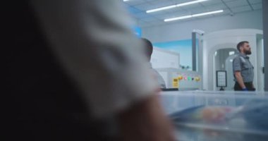 Havaalanı Güvenlik Kontrol Noktası: Afrikalı Amerikan Güvenlik Subayı Bilgisayar ekranlarında bagaj taramasını izliyor. Kişisel Malzemeleri Tepsilere Koyan Yolcular, Uçuştan Önce Oluk Metal Detektöründen Geçtiler.