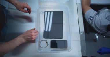 Kişisel Ögeleri Plastik Tepsiye yerleştiren Yolcuların En İyi Görünümü: Tablet Bilgisayar, Telefon, Çanta. Uçağa binmeden önce havaalanı güvenliği kontrol noktası. Güvenlik Subayı Prosedürü Denetliyor.